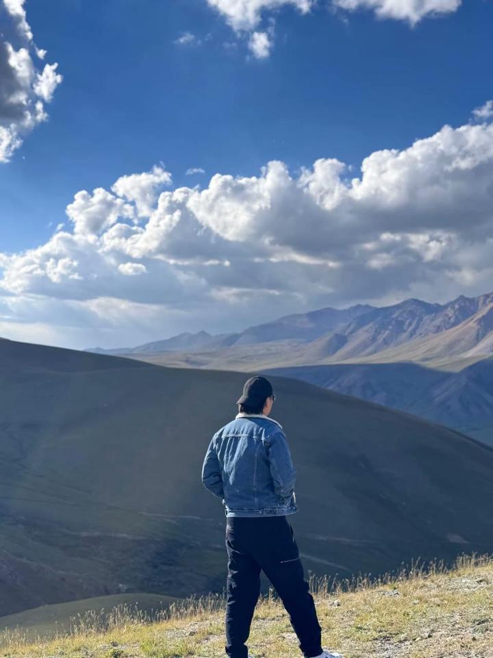 John Carrie from behind in a denim jacket and cap, looking out over mountains.